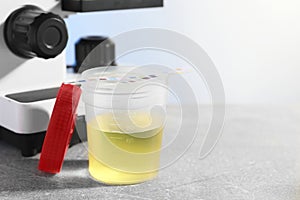 Container with urine sample for analysis and test strips on grey table in laboratory, space for text