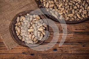 The container on the wood grain table is full of peanuts