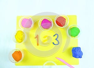 Containers with colorful plasticine and the child made numbers one , two, three.  white  wooden background