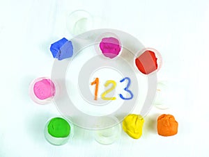 Containers with colorful plasticine and the child made numbers one , two, three.  white  wooden background.