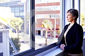 Contemplating her vision for the company. a thoughtful businesswoman looking out of an office window.