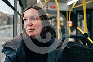 Contemplative adult caucasian woman riding public transportation bus through city streets