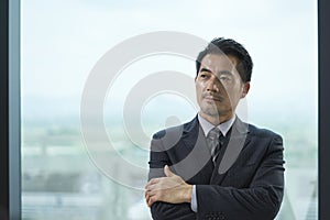 Contemplative asian business man standing by windwo in office