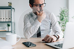 Contemplative caucasian businessman looking at laptop computer screen in business office