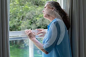 Contemplative caucasian senior woman looking away while standing at window in house