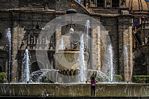 Contemplative little girl in front of the fountain of the Guadalajara Cathedral, Jalisco, Mexico