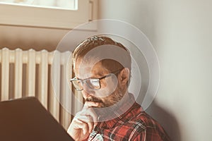 Contemplative man reading a book at home, sitting by the window