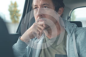 Contemplative man wearing light gray sweatshirt with hoodie sitting at the back seat of the car and thinking