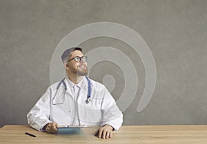 Contemplative satisfied doctor sitting at desk holding clipboard studio shot