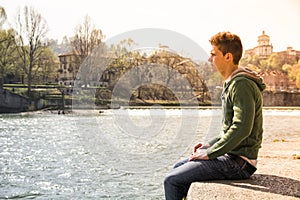 Contemplative teenage boy sitting beside river