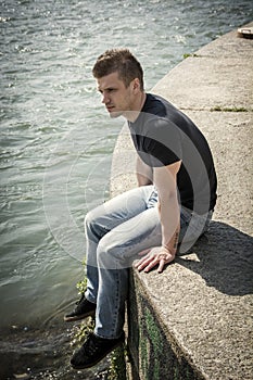 Contemplative teenage boy sitting beside river
