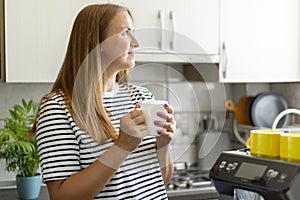 Contemplative woman holding a coffee mug in a sunlit kitchen