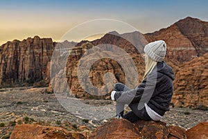 Contemplative Woman sitting on a rock ledge overlooking beautiful Snow Canyon State park in the deserts of Utah enjoying the view