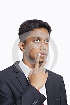 Contemplative young Asian businessman with hand on chin against white background