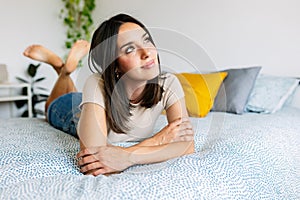 Contemplative young beautiful woman daydreaming on bedroom