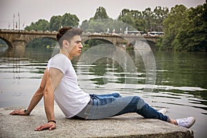 Contemplative young man sitting beside river