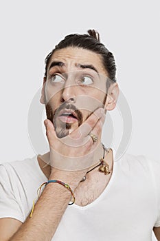 Contemplative young man in white t-shirt with hand on face against white background