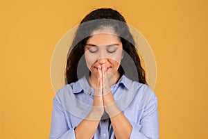 Contemplative young woman with eyes closed and hands pressed together in a prayerful