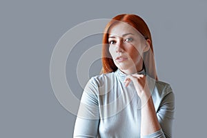 contemplative young woman with long red hair and light blue turtleneck