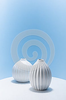 Contemporary art still life with white ceramic vases on pastel blue wall, white table with shadow, vertical. Simple elegance.