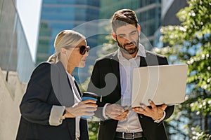 Contemporary businessman and businesswomen working outdoor on laptop with new startup project