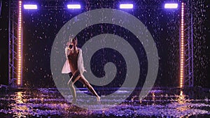 Contemporary dance ballerina dances sensually in rain on water surface, creating splashes. Silhouette of wet woman in