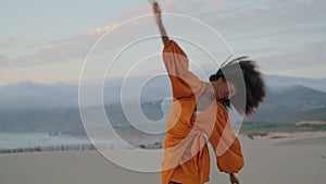 Contemporary dancer waving hands performing on sand seashore summer evening.