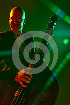 Contemporary double bass player in silhouette in red-green neon light against gradient studio background.