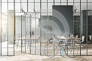 Contemporary glass partition and bike in stylish coworking office interior with empty black mock up poster and city view and
