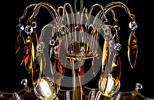 Contemporary gold chandelier isolated on black background. Crystal chandelier decorated amber crystals close-up