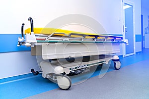 Contemporary hospital bed on wheels with yellow mattres in light white and blue hall.