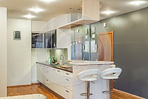 Contemporary interior of kitchen in luxury flat. Modern kitchen set with sink. Wooden counter. White walls. Bar stools.