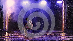 Contemporary modern dance ballerina moves sensually in the rain, sitting on chair. Silhouette of a wet woman in a white