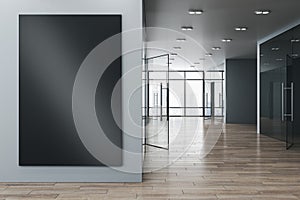 Contemporary new office corridor interior with glass windows and city view, wooden flooring and empty black mock up poster on wall