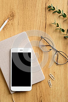 Contemporary office desk top view. Flat lay smartphone with blank screen mockup, paper notebook, glasses, feminine glasses,