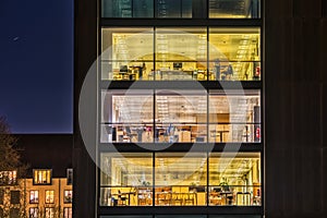 A contemporary office with a broad modern, glazed facade featured by square pattern of wide glazed windows illuminated at night