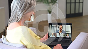 Contemporary senior woman sitting on armchair and using laptop for video connection