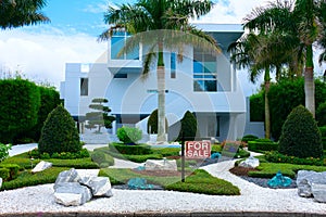 Contemporary tropical mansion house with palm trees and zen garden with FOR SALE sign in the front yard
