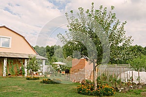 Contemporary two-story house in countryside in summer with fruit trees, flowers, vegetable garden and oven built for