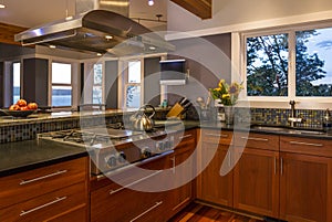 Contemporary upscale home kitchen interior with wood cabinets, gas stove, vent hood and view windows