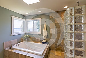 Contemporary upscale home spa bathroom interior with acrylic soaking tub , glass block shower, slate tile walls, and view windows