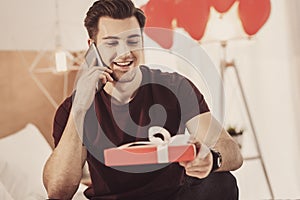 Contended young man preparing present for his wife while sitting in living room