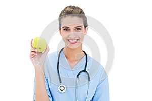 Content brown haired nurse in blue scrubs holding a green apple