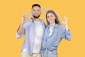 Content couple showing OK signs with hands, smiling on yellow background