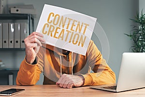 Content creation, man holding paper in front of his face in home office interior