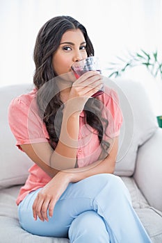 Content cute brunette sitting on couch drinking glass of juice