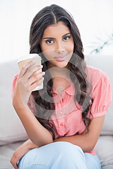 Content cute brunette sitting on couch holding disposable cup