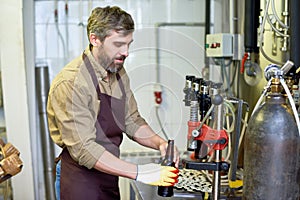 Content handsome technician putting beer in bottles at factory