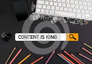 Content is king concept. On a black table colorful pencils and a computer keyboard with a mobile phone