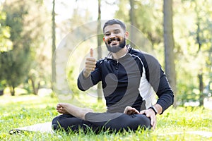 Content man giving thumbs up while meditating in park
